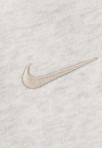 Le logo Nike brodé en beige sur un tissu gris clair doux avec une texture lisse, présentant un design courbé simple.