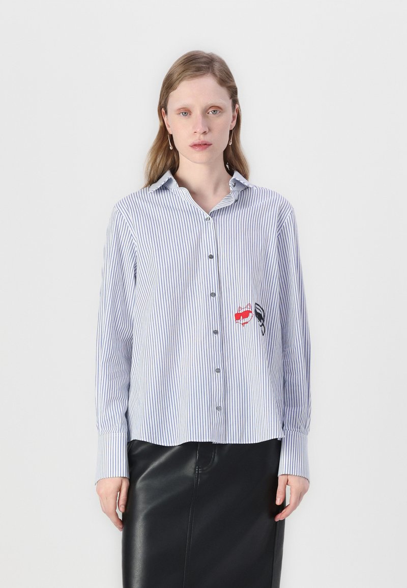Blue and white striped button-up shirt with long sleeves, featuring embroidered red lips and black accents on the left side.