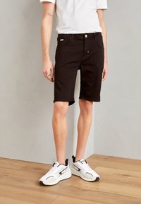 Pantalones cortos de mezclilla negra con corte recto, que cuentan con un cierre de botón frontal, bolsillos laterales y un dobladillo que termina justo por encima de la rodilla. Combinados con zapatillas blancas.
