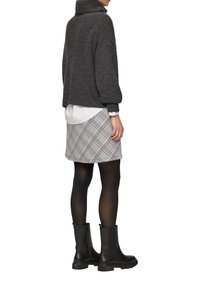 Szary, oversize sweter z wysokim kołnierzem, w zestawie z mini spódniczką w kratę w odcieniach kremowym i czarnym oraz czarnymi botkami za kostkę z grubą podeszwą.