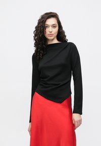 Czarna bluzka z długim rękawem, z dekoltem typu łódka i drapowanym przodem, zestawiona z żywą czerwoną spódnicą o gładkiej fakturze.