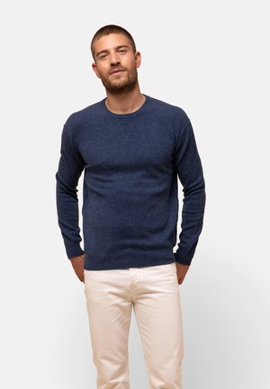 Mørkeblå sweater lavet af blødt strikket stof med lange ærmer og rund halsudskæring, parret med lyse bukser. Simpelt design, ingen mønstre.