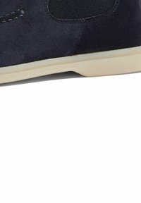 Zapato de ante azul marino con acentos elásticos en los laterales y suela de goma. Presenta una textura suave y un detalle de costura minimalista.