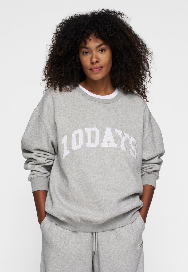 Grauer Pullover mit "10 DAYS" in Weiß bedruckt. Aus weichem Stoff gefertigt, mit Rundhalsausschnitt und gerippten Bündchen, kombiniert mit passenden grauen Hosen.