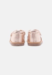 Μεταλλικά παπούτσια νηπίων σε ροζ χρυσό με κλειστή φτέρνα και καφέ λαστιχένια σόλα, απεικονίζονται από πίσω σε λευκό φόντο.