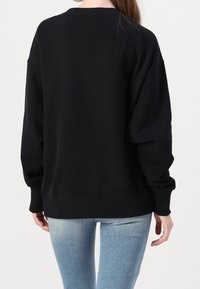 Svart sweatshirt med en avslappnad passform, vida ärmar och ribbat krage. Materialet verkar mjukt; nederkanten är något längre, utan synliga mönster.