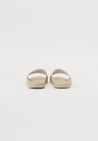 Beige Schlüpfsandalen mit glatter Textur, offenem Rücken und zwei oberen Riemen. Flache Sohle, minimalistisches Design, geeignet für den Freizeitlook.