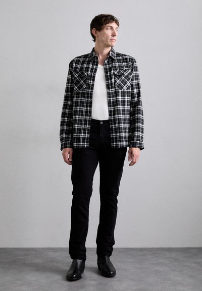 Μαύρο και άσπρο καρό πουκάμισο με δύο τσέπες στο στήθος, φορεμένο πάνω από άσπρη μπλούζα με λαιμόκοψη, σε συνδυασμό με μαύρα τζιν και μαύρες μποτάκια μέχρι τον αστράγαλο.