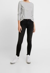 Graues langärmliges Oberteil mit rundem Ausschnitt, schwarze Skinny-Jeans und weiße High-Top-Sneaker mit Schachbrettmuster auf der Sohle.