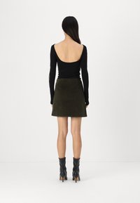 Top negro de manga larga con la espalda baja, combinado con una falda de ante verde oliva. La modelo completa el look con botas de tacón negro hasta el tobillo.