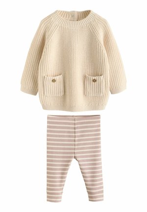 Gestrickter cremefarbener Pullover mit zwei vorderen Taschen und gerippten Bündchen, kombiniert mit hellpinken und cremefarbenen gestreiften Leggings.