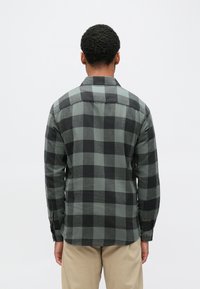 Camisa xadrez verde e preta com colarinho, mangas compridas e punhos com botões. Confeccionada em tecido de textura macia. Detalhes de costura visíveis.