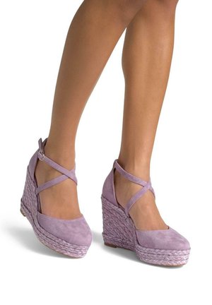 Le décolleté in suede viola presentano una zeppa in juta intrecciata e cinghie alla caviglia incrociate, offrendo un contrasto di texture rispetto al materiale superiore liscio.