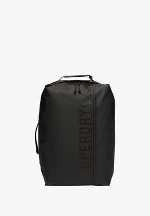 Mochila impermeable negra con un acabado mate, que presenta un logotipo vertical prominente, dos bolsillos laterales y un asa superior para transportar.