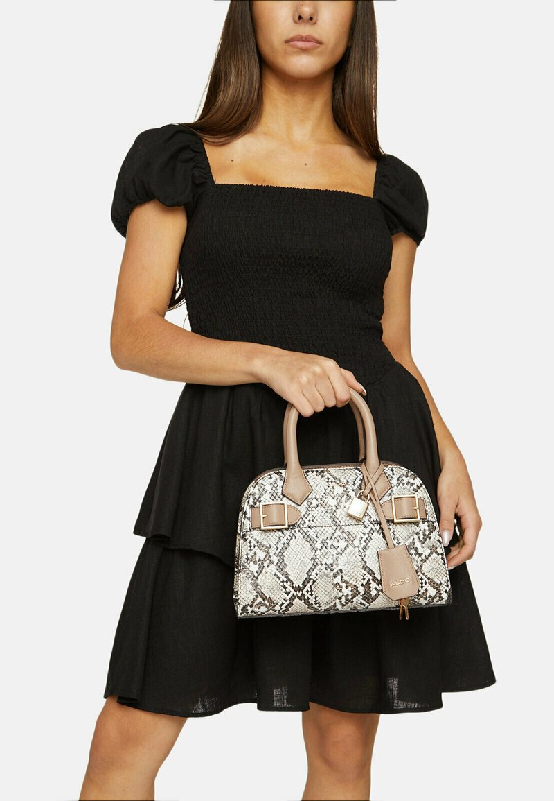 Sac en cuir avec motif serpent et accents beiges, forme structuré et doubles anses supérieures. Porté avec une robe noire à manches bouffantes.