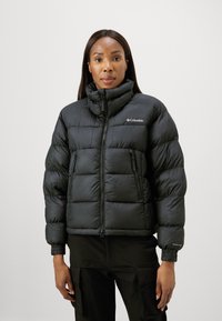 Geacă puffer neagră cu guler înalt, fermoar frontal și manșete elastice. Prezintă o textură moale, matlasată și logo-ul Columbia pe piept.