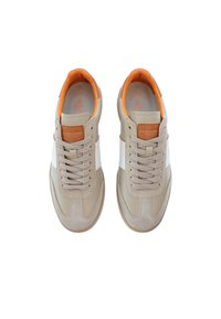 Beige sneakers med en slät läderovandel, vit sidopanel, orange inredning och grå snören. Har ett brunt läderemblem på tungan.