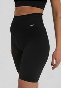 Pantaloni corti neri a vita alta realizzati in tessuto texturizzato, con un design aderente e un piccolo logo argento sul cinturino.