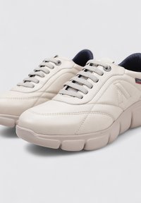 Zapatillas de cuero beige con punta redondeada, diseño texturizado y cordones grises. Suela de goma gruesa y cuello acolchado.