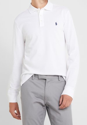 Witte polo met lange mouwen en een klassieke kraag, met een klein marineblauw logo op de borst. Gecombineerd met grijze broek.