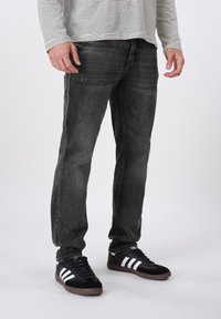 Μαύρα τζιν από τζιν με ελαφρύ ξεθώριασμα και φθαρμένες λεπτομέρειες, σε συνδυασμό με μαύρα αθλητικά παπούτσια με λευκές ρίγες και καφέ ελαστική σόλα.