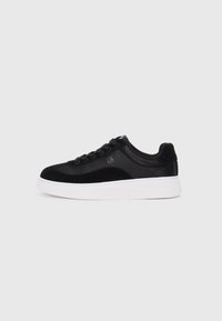 Black sneaker with suede and synthetic materials, round toe, black laces, white rubber sole, and logo detail on the side.
