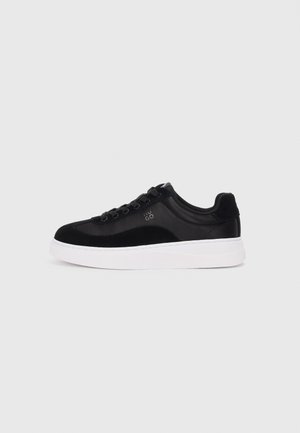 Black sneaker with suede and synthetic materials, round toe, black laces, white rubber sole, and logo detail on the side.
