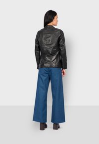 Černá kožená bunda s propracovaným střihem, v kombinaci s širokými modrými džínovými kalhotami a robustními hnědými botami na podpatku. Jednoduchý, moderní design.