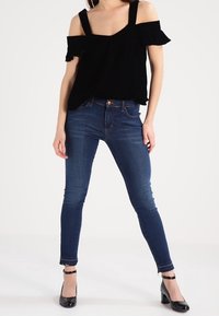 Svart axelbandslös topp med volangärmar, kombinerad med mörkblå smala jeans och svarta klackskor med remmar runt ankeln.