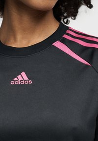 Μαύρο αθλητικό τοπ με λαιμόκοψη crew, με ροζ τρεις ρίγες στους ώμους και κεντημένο ροζ λογότυπο Adidas.