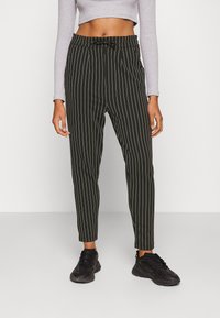 Calças listradas em preto e branco com um corte ajustado, apresentando um detalhe de laço na cintura. O material parece suave e leve.