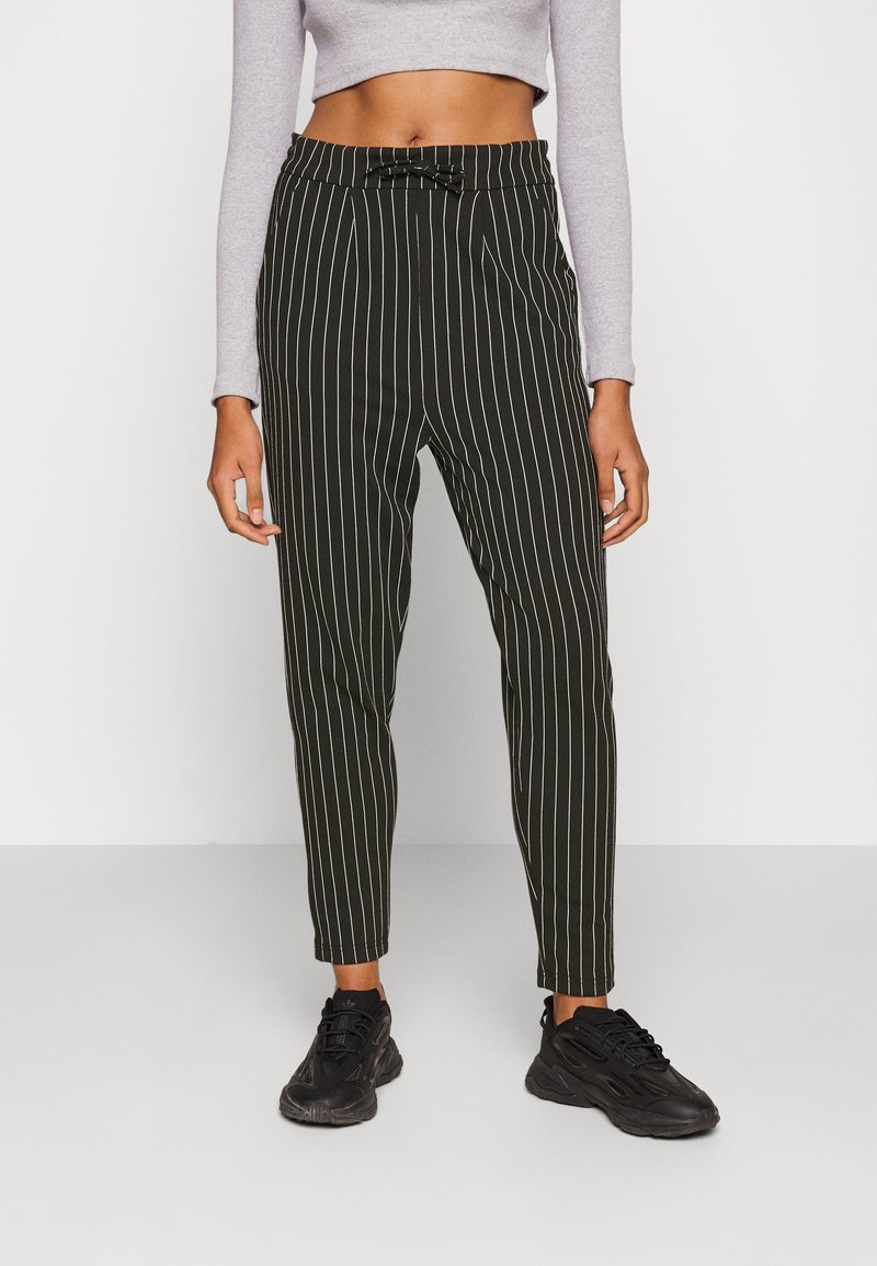 Calças listradas em preto e branco com um corte ajustado, apresentando um detalhe de laço na cintura. O material parece suave e leve.