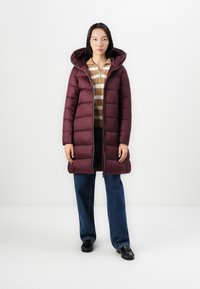 Bordeaux puffer jas met capuchon, voorzien van een ritssluiting aan de voorkant en segmentgestikte naden, gedragen over een gestreepte trui en gecombineerd met wijde spijkerbroek.