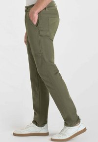 Pantalons vert olive en coton, avec poches avant et détails de couture. Associés à des baskets blanches et un haut uni.