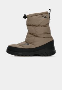 Botte beige rembourrée avec semelle en caoutchouc noir et accents texturés. Elle est dotée d'une fermeture à cordon et de détails de logo, conçue pour les conditions météorologiques froides.