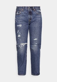 Pantalones vaqueros de denim en un lavado intermedio con detalles desgastados, incluyendo desgarros y deshilachados en las rodillas, con un corte recto y diseño de cinco bolsillos.