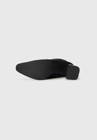 Chaussure à talon haut en suède noir avec une pointe arrondie et un talon rectangulaire. La semelle est en caoutchouc texturé pour une meilleure adhérence et durabilité.