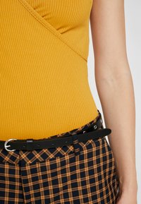 Ribbade senapsgula linne ihop med blå och senapsgula rutig byxor, accentuerat med ett smalt svart bälte med silverfästen.