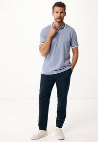 Polo shirt azzurro chiaro con rifiniture bianche a contrasto col colletto e le maniche, abbinato a pantaloni navy scuri e sneakers bianche.