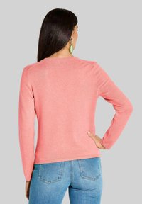 Roze gebreide trui met lange mouwen en een ronde hals. Beschikt over geribde manchetten en zoom, een gladde textuur en een getailleerde pasvorm.