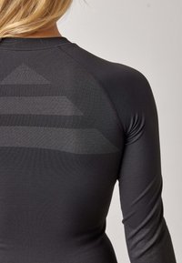 Black long-sleeve athletic shirt with a textured pattern on the back featuring triangular shapes, made from a smooth, stretchy material.