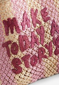 Bolso de ganchillo en tonos rosa y beige con texto bordado en relieve que dice "HAZ DE HOY UNA HISTORIA." El texto tiene una apariencia texturizada y aterciopelada.