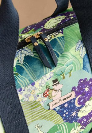 Reusable tote bag in patterned fabric featuring flora and Moomin characters. Blue zip with gold hardware, navy handles, and brand tag visible.
