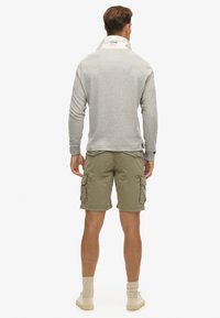 Lichtgrijze langemouwen pullover met een hoge kraag en een witte binnenkant, gecombineerd met olijfgroene cargoshorts met meerdere zakken.