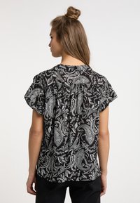 Sort bluse med hvid paisley-mønster, korte ærmer og plisseret rygdetalje. Fremstillet af letvægtsstof.