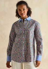 Colorful floral patterned button-up shirt with a blue striped collar and cuffs, made of a lightweight fabric. Features long sleeves and a relaxed fit.