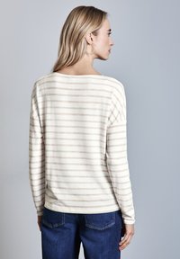 Cremfarbene und beige gestreifte Langarmbluse mit lockerer Passform, Rundhalsausschnitt und weichem Textil, kombiniert mit dunkelblauen Jeans.