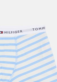 Biele a svetlomodré pruhované boxerky s bielym elastickým pásom, na ktorom je logo a vlajkový emblém Tommy Hilfiger.
