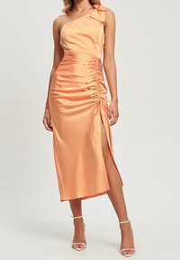 Robe en satin à une épaule de couleur orange clair, avec des fronces sur le côté, un accent noué à l'épaule et une fente haute sur la cuisse.