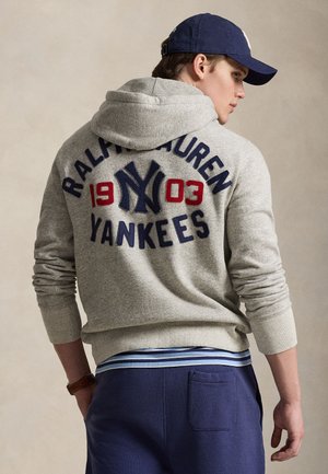 Γκρι φούτερ με κουκούλα, στο πίσω μέρος έχει μεγάλο κεντητό λογότυπο «New York Yankees» σε ναυτικό μπλε και κόκκινο. Συνοδεύεται από ναυτικό μπλε παντελόνι.